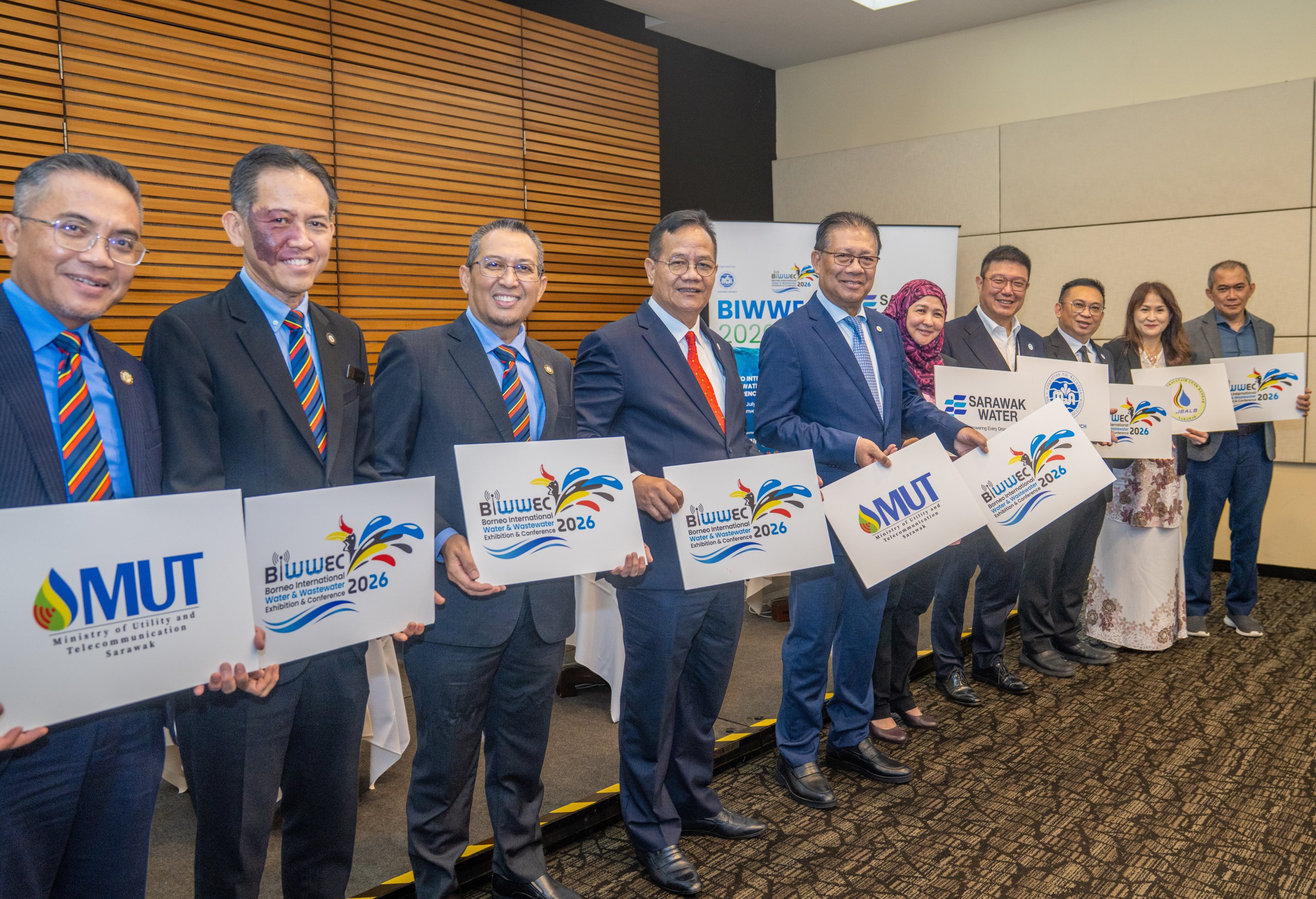 Group of professionals in suits posing with BIWEC 2026 banners at an indoor event central to the photo.