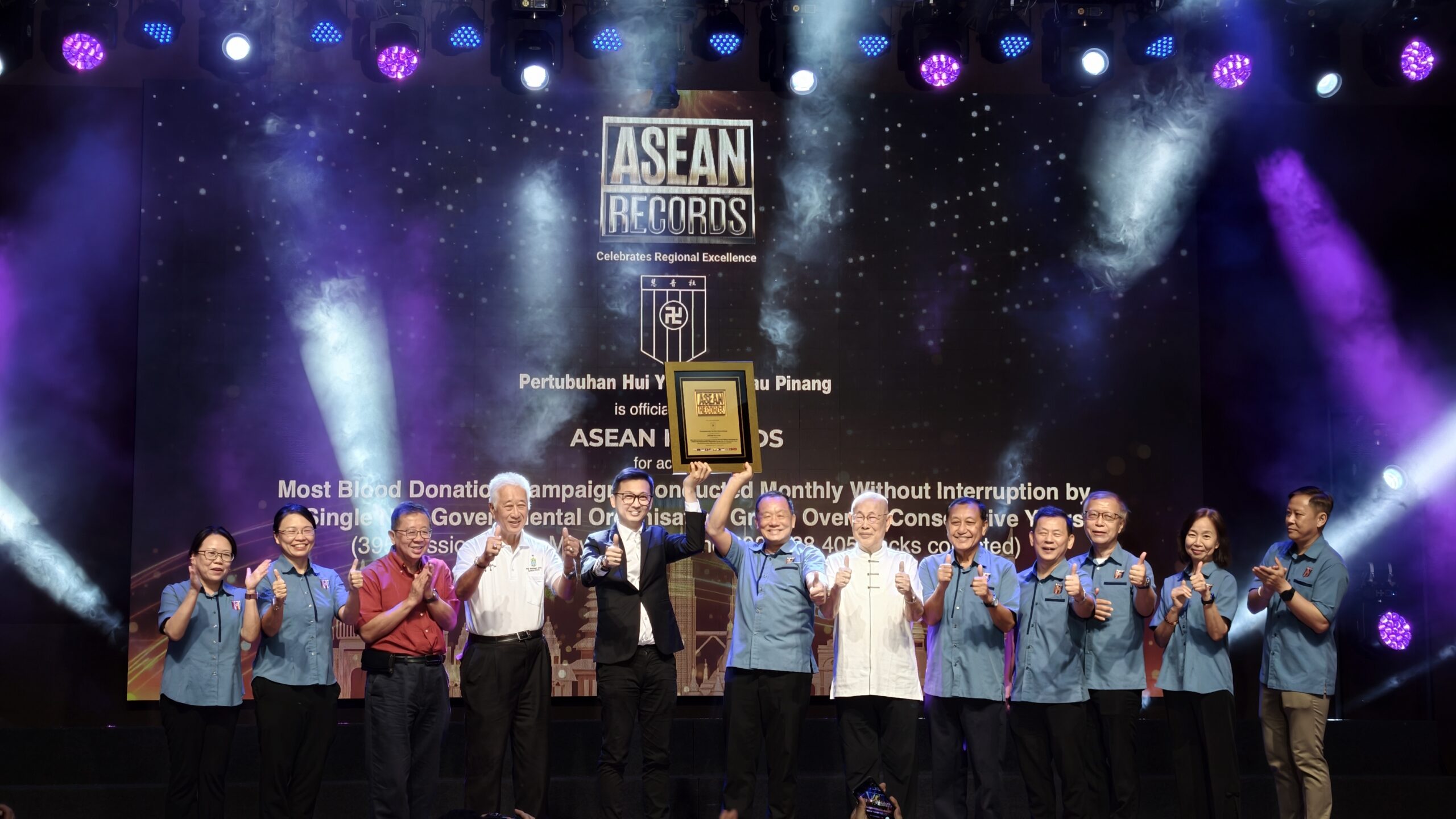 Group of people on a stage giving thumbs up, holding a framed award under a banner that reads 'ASEAN RECORDS'.