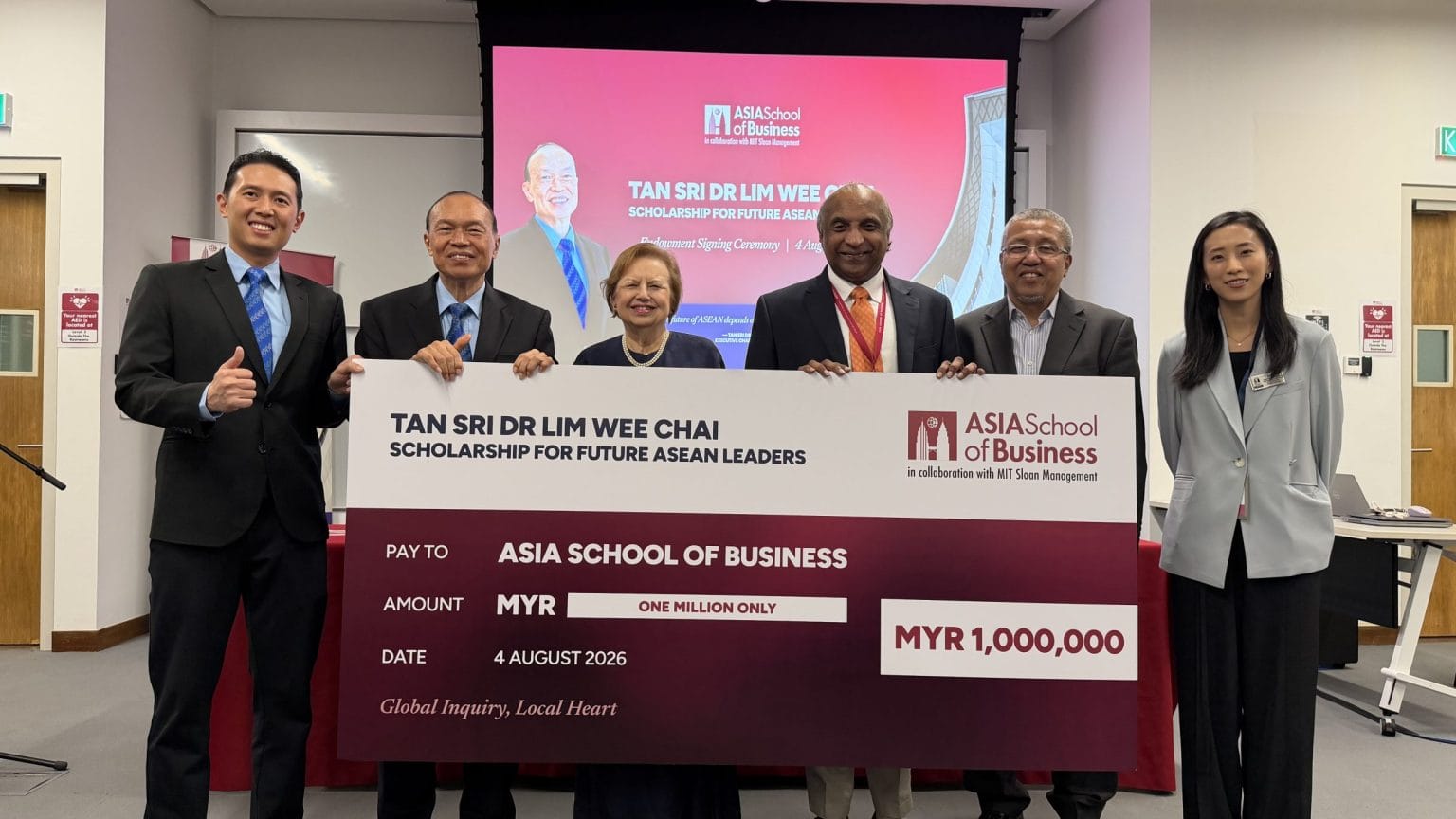 Group of six professionals posing with a large ceremonial cheque for MYR 1,000,000 from the Asia School of Business and a scholarship announcement in a conference room.