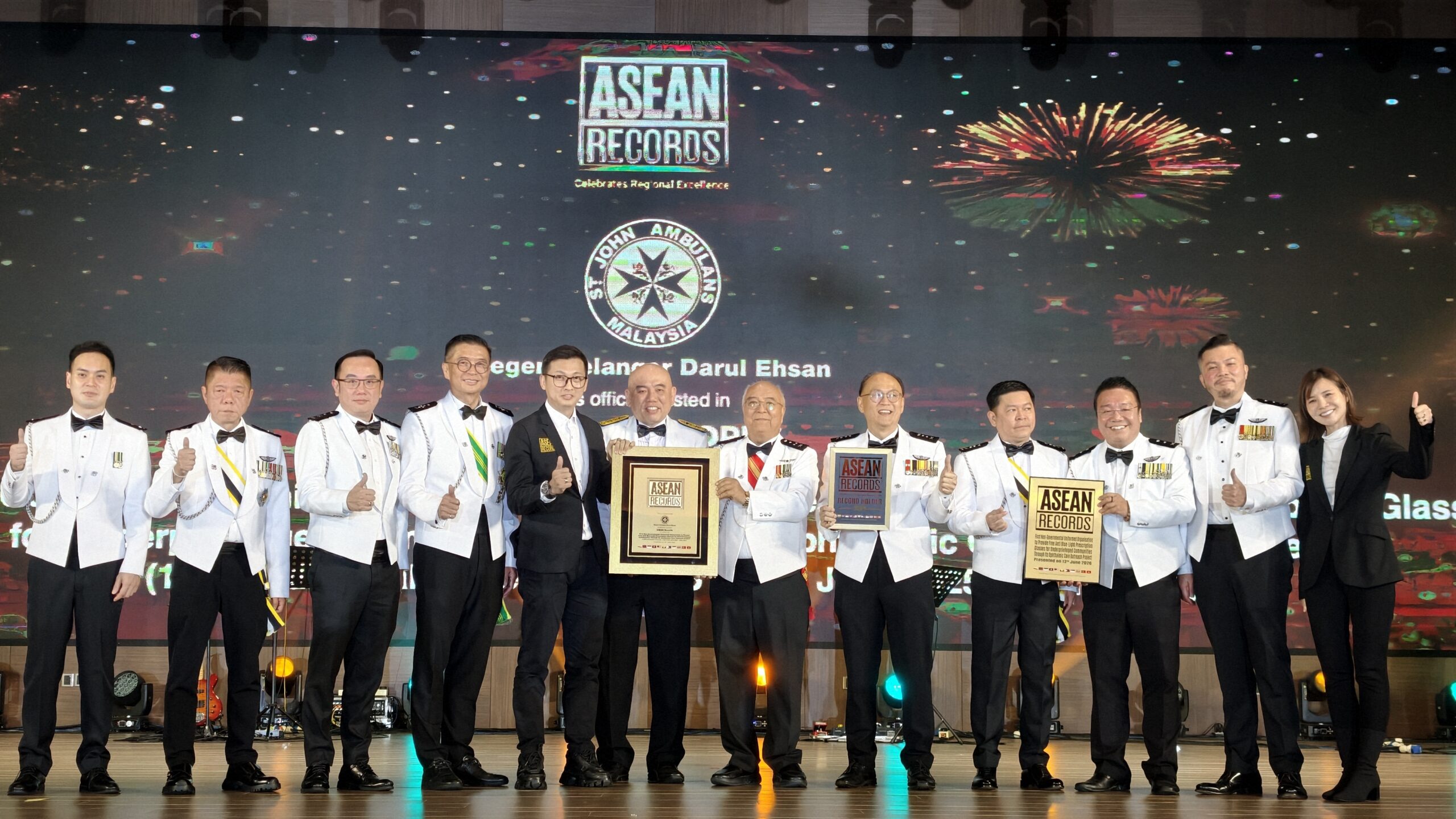 Group of awardees in white uniforms on stage, holding plaques and certificates at an ASEAN Records ceremony.